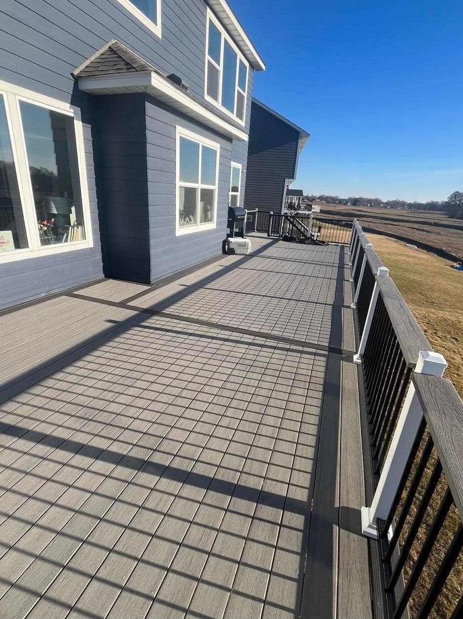 Modern gray deck with railing, sunlight casting shadows, overlooking open grassy area.