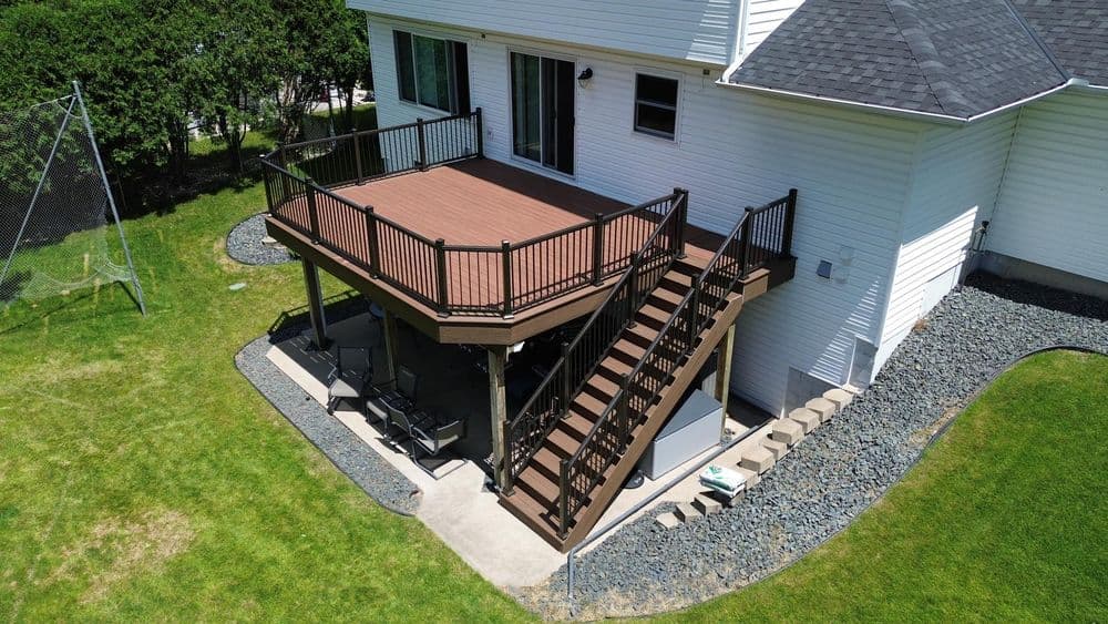 Spacious outdoor deck with stairs, surrounded by green lawn and gravel pathway.