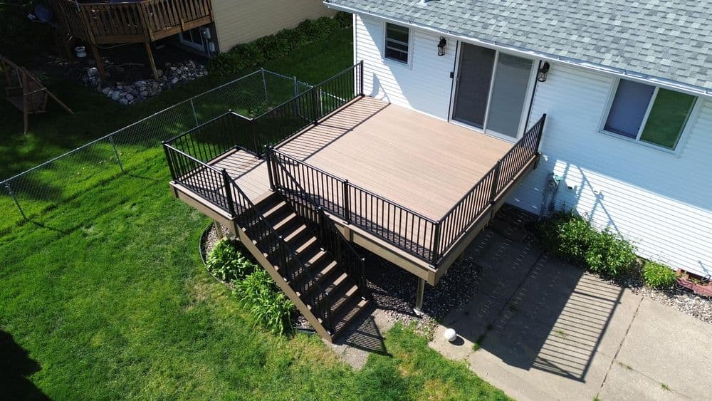 Aerial view of a spacious wooden deck with black railings and stairs, surrounded by green grass.