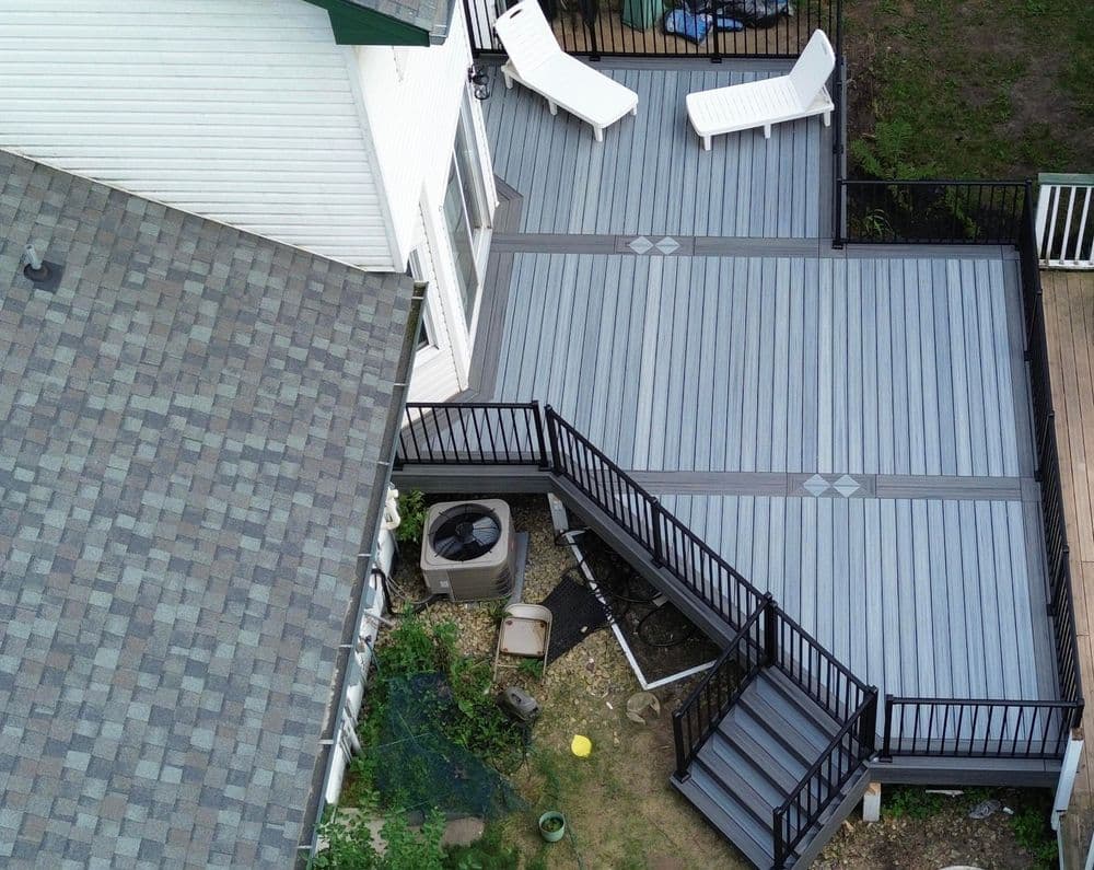 Aerial view of a gray deck with railings, two white chairs, and surrounding landscaping.